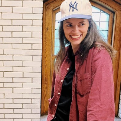 Mac smiling in a cream New York Yankees cap and a rust-red overshirt